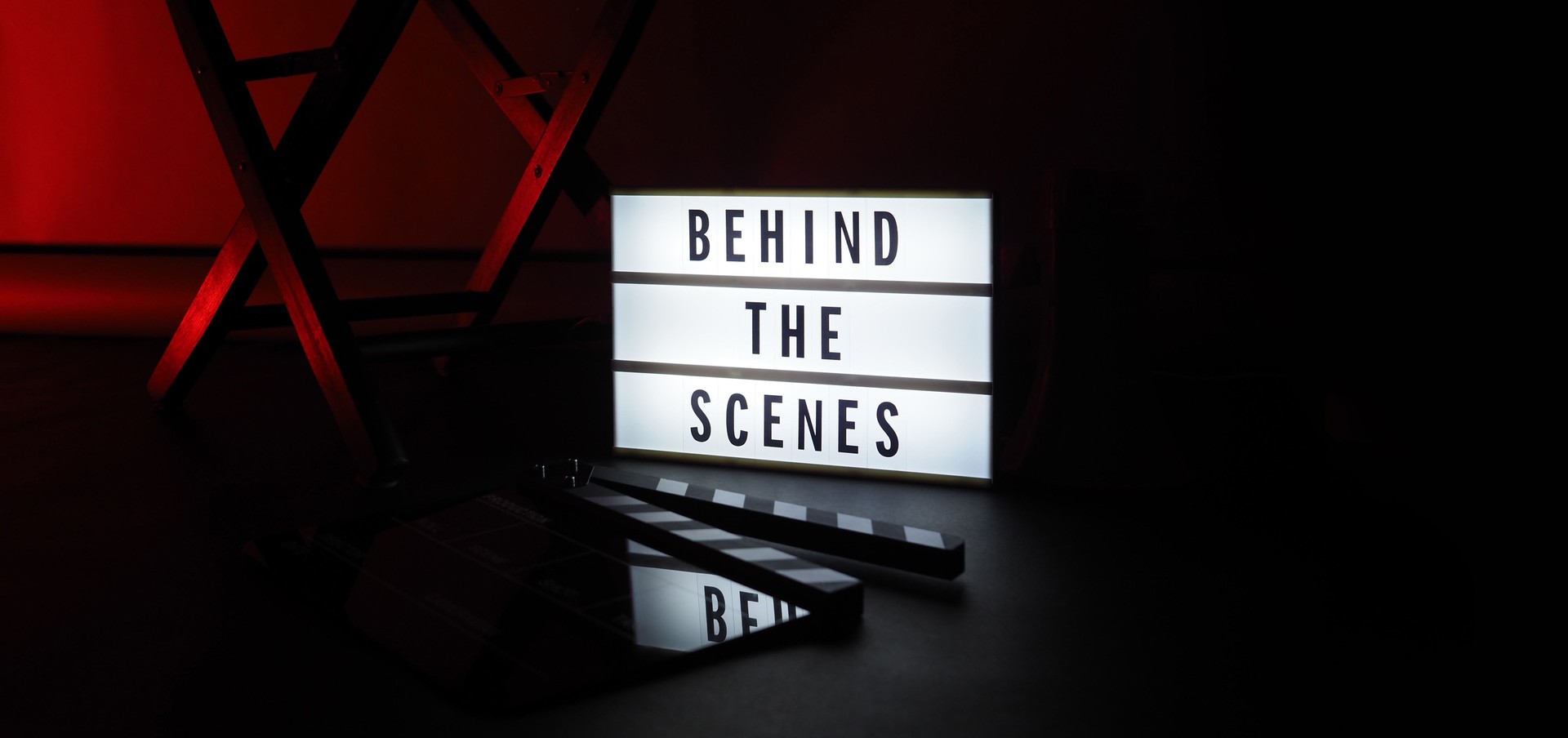 Behind the scenes letterboard text on Lightbox or Cinema Light box. Movie clapperboard megaphone and director chair beside. Background LED color change loop. static camera in video production studio.